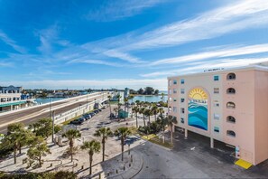 A beachfront hotel with a mural of a sun and waves, a parking lot, and a view of the beach and ocean.