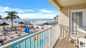 Un balcon avec une piscine donnant sur une plage équipée de chaises longues et de parasols.