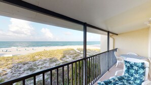 A balcony with a view of a beach and ocean. There is a table and two chairs. - Beach Front 1B1B Balcony 2 Beds - Surf Song #349 (Madeira Beach)