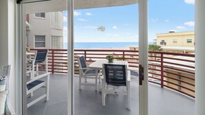 Un balcon avec une table et des chaises, donnant sur une plage et un immeuble.