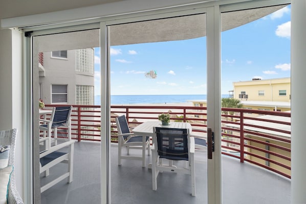 A balcony with a table and chairs, overlooking a beach and a building.
