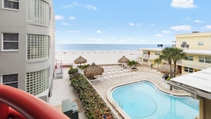 Un espace piscine avec vue sur la plage, un bâtiment à la façade incurvée et un palmier.