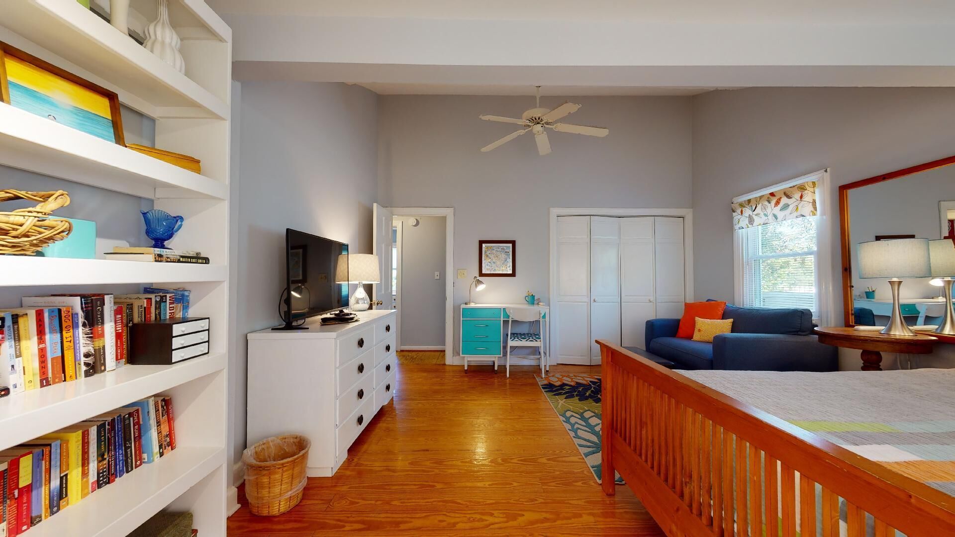 A spacious living room with a TV, bookshelf, and a desk.