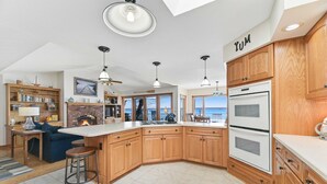 A modern kitchen with wooden cabinets, a large island, and a view of the ocean. - Russell's Rendezvous - Enjoy a Vacation Full of Adventure! (Dresden)