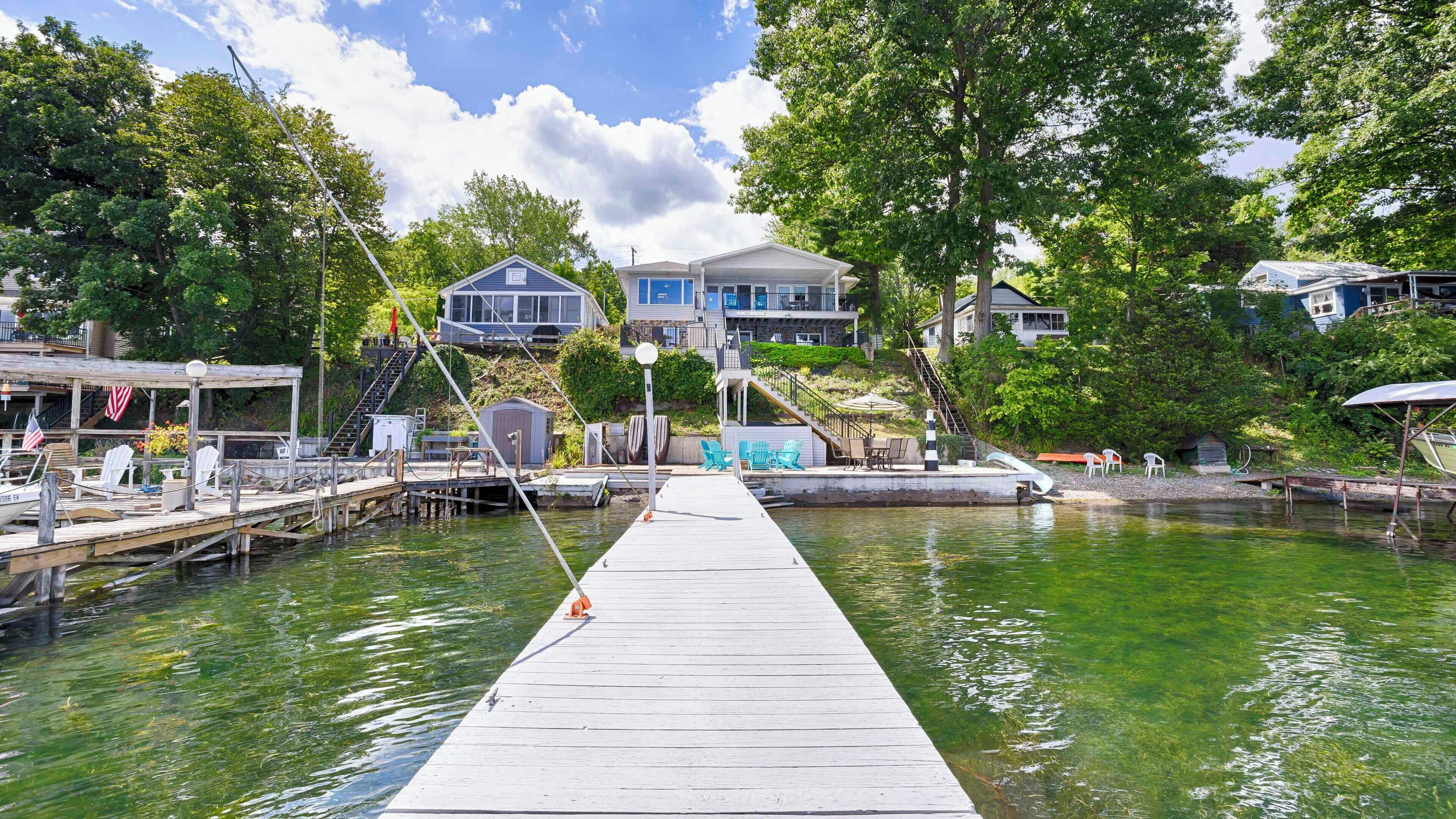 Eine hölzerne Pier, die sich in einen See erstreckt, mit einem Boot am Steg und Stühlen auf der linken Seite.