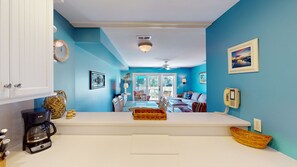 A bright room with a white counter, a coffee maker, and a basket. There is a door on the left and a window on the right.
