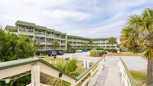 A multi-story hotel with a green roof, a parking lot, and a wooden walkway leading to the entrance.