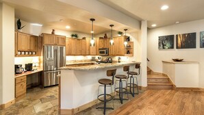 A modern kitchen with wooden cabinets, stainless steel appliances, and a central island with bar stools. - Largest Black Bear Townhome - Ping Pong Table - on Demand Ski Shuttle (Durango)