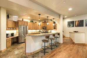 Une cuisine moderne avec des meubles en bois, des appareils en acier inoxydable et un îlot central doté de tabourets de bar.