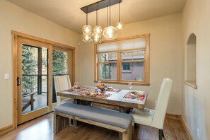 A dining area with a wooden table, chairs, and a bench. There are windows with views of trees and a building. - Largest Black Bear Townhome - Ping Pong Table - on Demand Ski Shuttle (Durango)