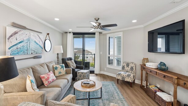 A spacious living room with a sofa, armchairs, a coffee table, a TV mounted on the wall, and a ceiling fan. - Beautiful oceanfront condo overlooking the pool and beach in Wild Dunes (Isle of Palms)