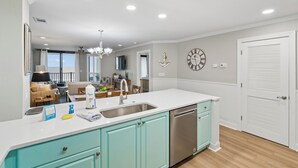 A kitchen with a sink, dishwasher, teal cabinets, and a clock on the wall. - Beautiful oceanfront condo overlooking the pool and beach in Wild Dunes (Isle of Palms)