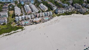 Vue aérienne d’une station balnéaire comprenant plusieurs bâtiments d’hôtel, un espace piscine central et une plage de sable.