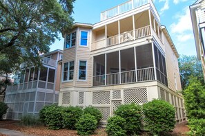 A two-story house with a balcony on the second floor, a porch with lattice railings, and a screened porch on the first floor. - Beautifully decorated home in Wild Dunes with beach access and rooftop deck (Isle of Palms)