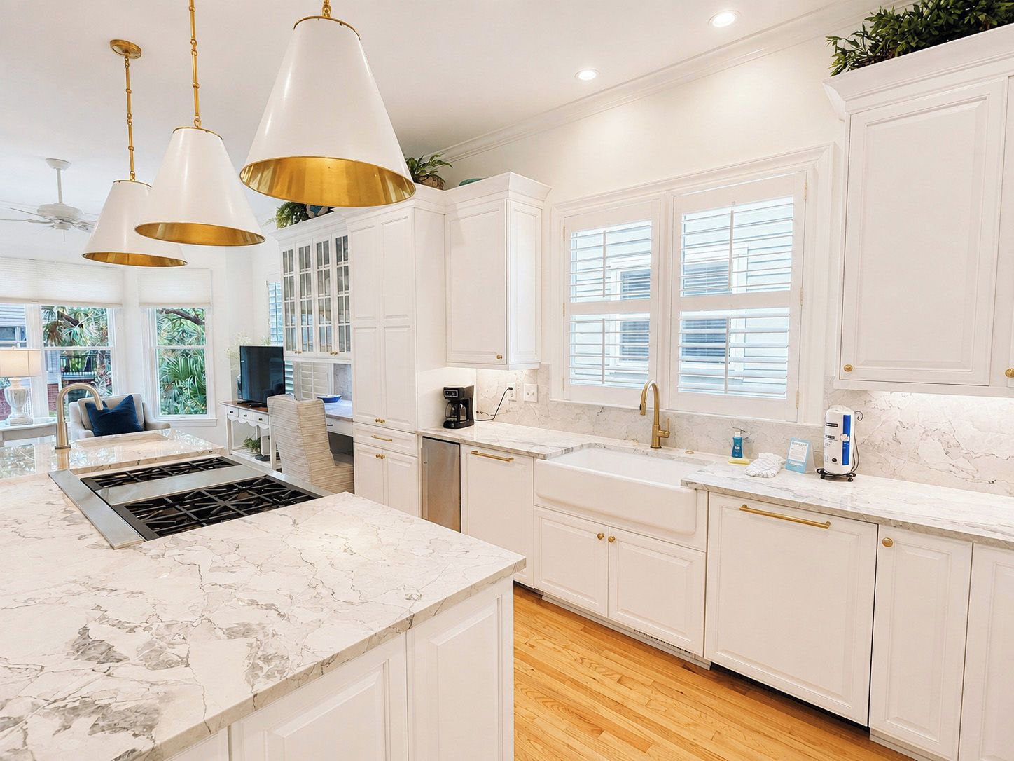 A modern kitchen with white cabinetry, marble countertops, and pendant lighting.