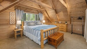 A cozy bedroom with a wooden ceiling, a bed with a blue-striped bedspread, a wooden bench, and a bedside table with a lamp. - Thyme Out/ HotTub, WIFI, Fenced Dog Space, Forest (Leavenworth)