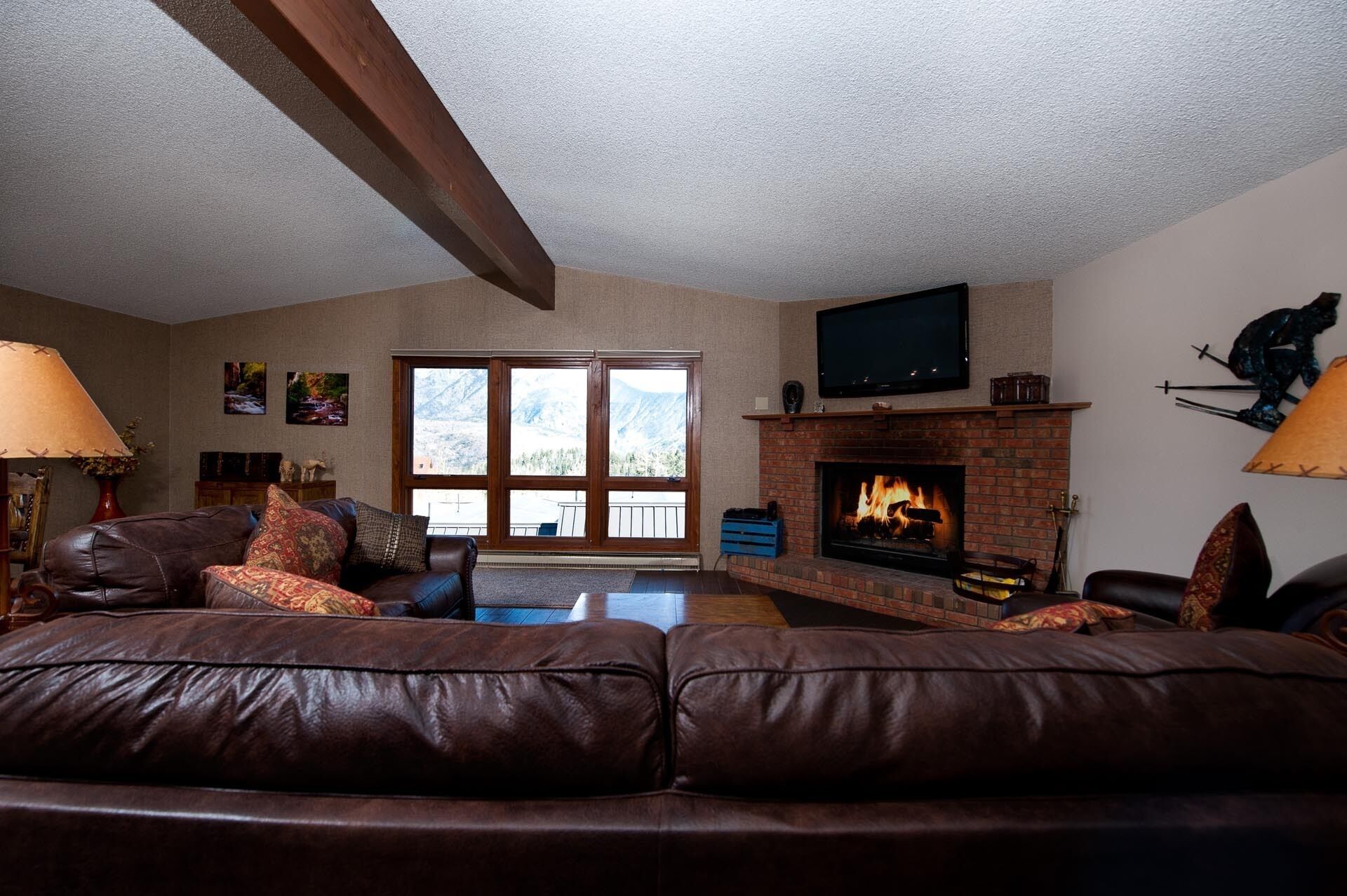 A living room with a fireplace, leather couches, a television, and a view of mountains through large windows.