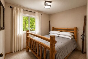 A bedroom with a wooden bed frame, a window with curtains, and a ceiling light fixture.