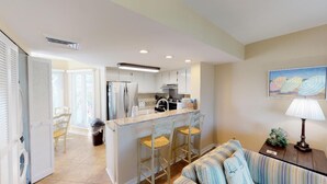 A modern kitchen with white cabinets, a central island with bar stools, and a dining area with striped cushions. - Wild Dunes condo with ocean views and sundeck (Isle of Palms)