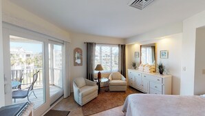A hotel room with a balcony, a bed, a desk, a chair, a dresser, and a lamp. - Wild Dunes condo with ocean views and sundeck (Isle of Palms)