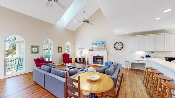 A spacious living room with a fireplace, a dining area with a round table, and a kitchen with white cabinets. - Traditional southern, pet friendly home (Isle of Palms)