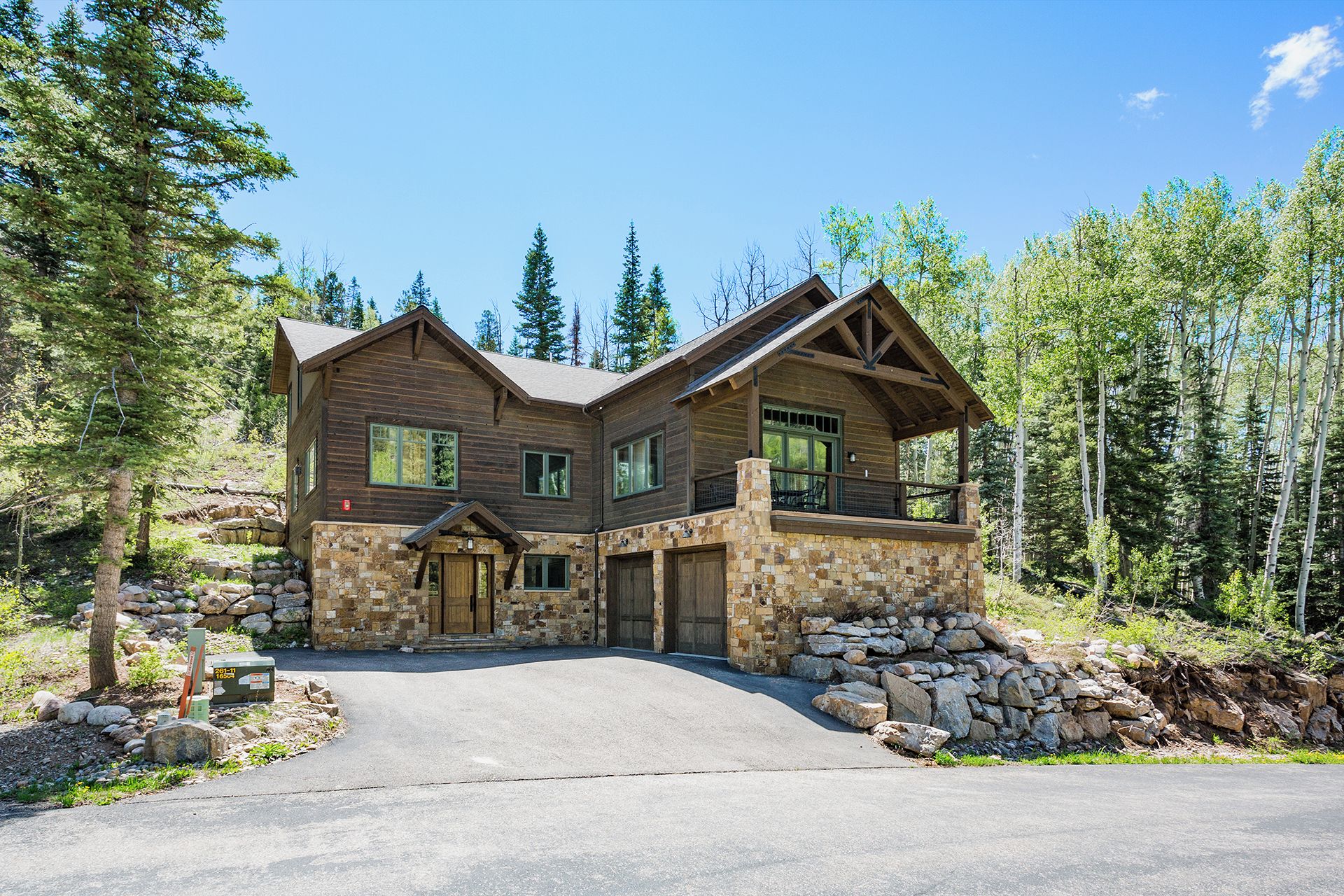 A two-story log cabin with a stone foundation, a front porch, and a stone retaining wall.