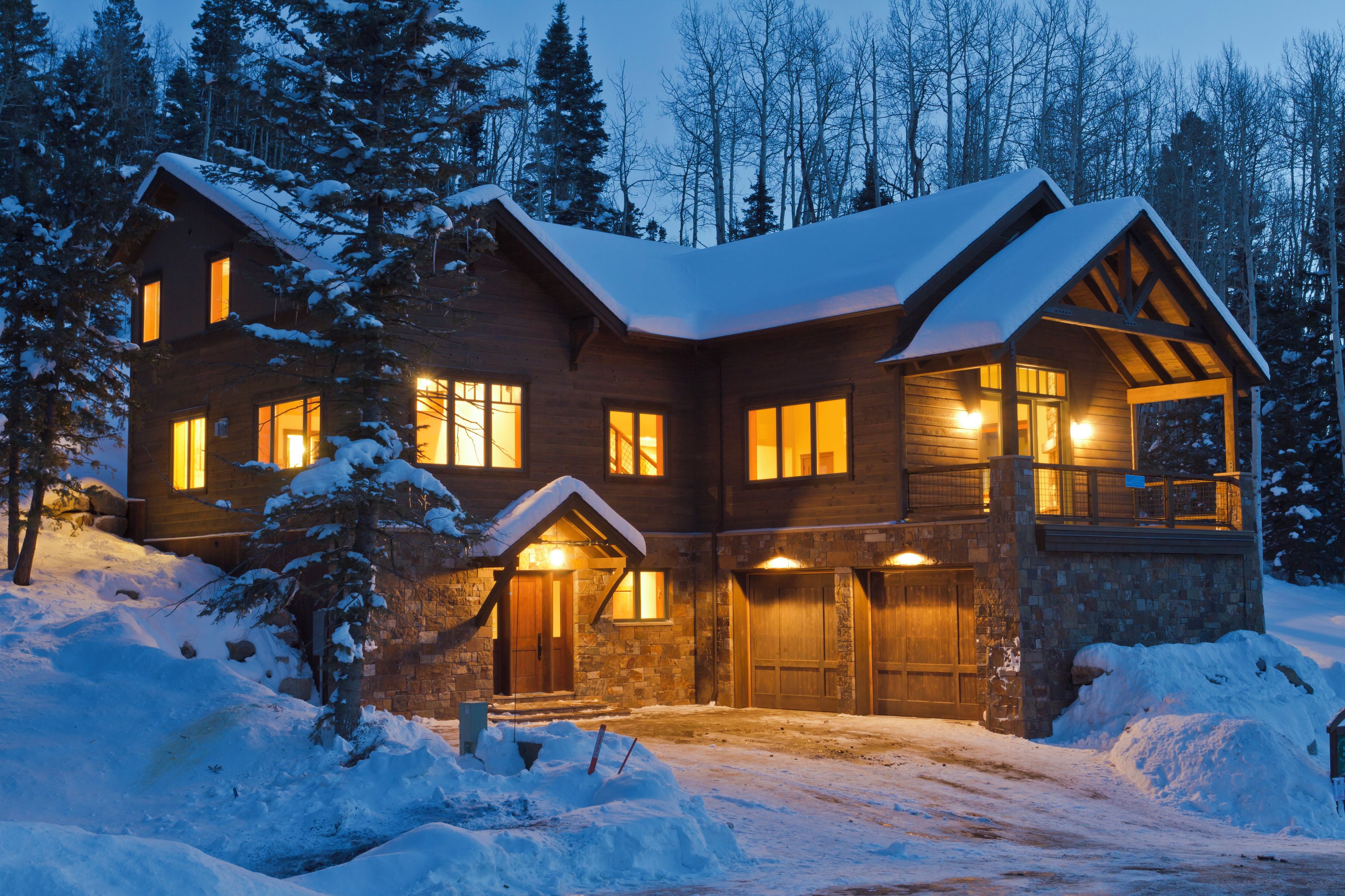 A large, two-story log cabin with multiple windows and a snow-covered roof, surrounded by a forest.