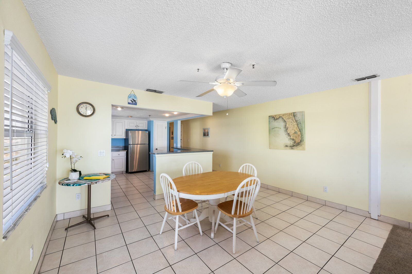 A compact kitchen with a refrigerator, a dining table with chairs, and a ceiling fan.