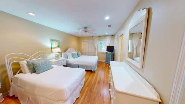 Habitación de hotel con dos camas, ventilador de techo, televisión y un espejo grande.