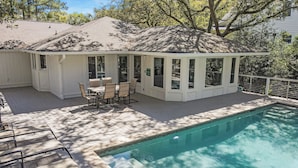 A covered patio with a pool, outdoor furniture, and a view of the surrounding trees.