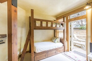 A bunk bed with a wooden frame and a white mattress, a small wooden bench, and a door leading to an outdoor seating area. - Large Comfortable Condo on 1 level, Spacious stone patio, 5 min to Skiing (Telluride)