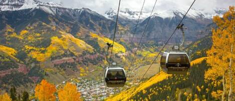 A cable car system in a mountainous area with autumn foliage and snow-capped peaks in the background.