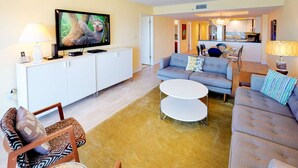 Una sala de estar moderna con un sofá, una mesa de centro, un televisor sobre un mueble blanco y un área de comedor al fondo.