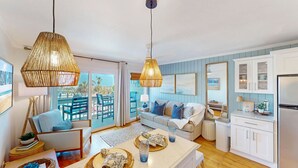 A spacious living room with a sofa, blue chairs, a dining table, and a kitchen area with cabinets and a refrigerator.
