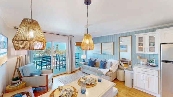 A spacious living room with a sofa, blue chairs, a dining table, and a kitchen area with cabinets and a refrigerator.