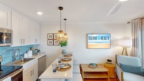 A modern kitchen with white cabinets, a blue backsplash, and a dining area with a bench and table.