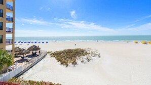 A beach with a clear sky, a sandy shore, and a building with balconies overlooking the beach.