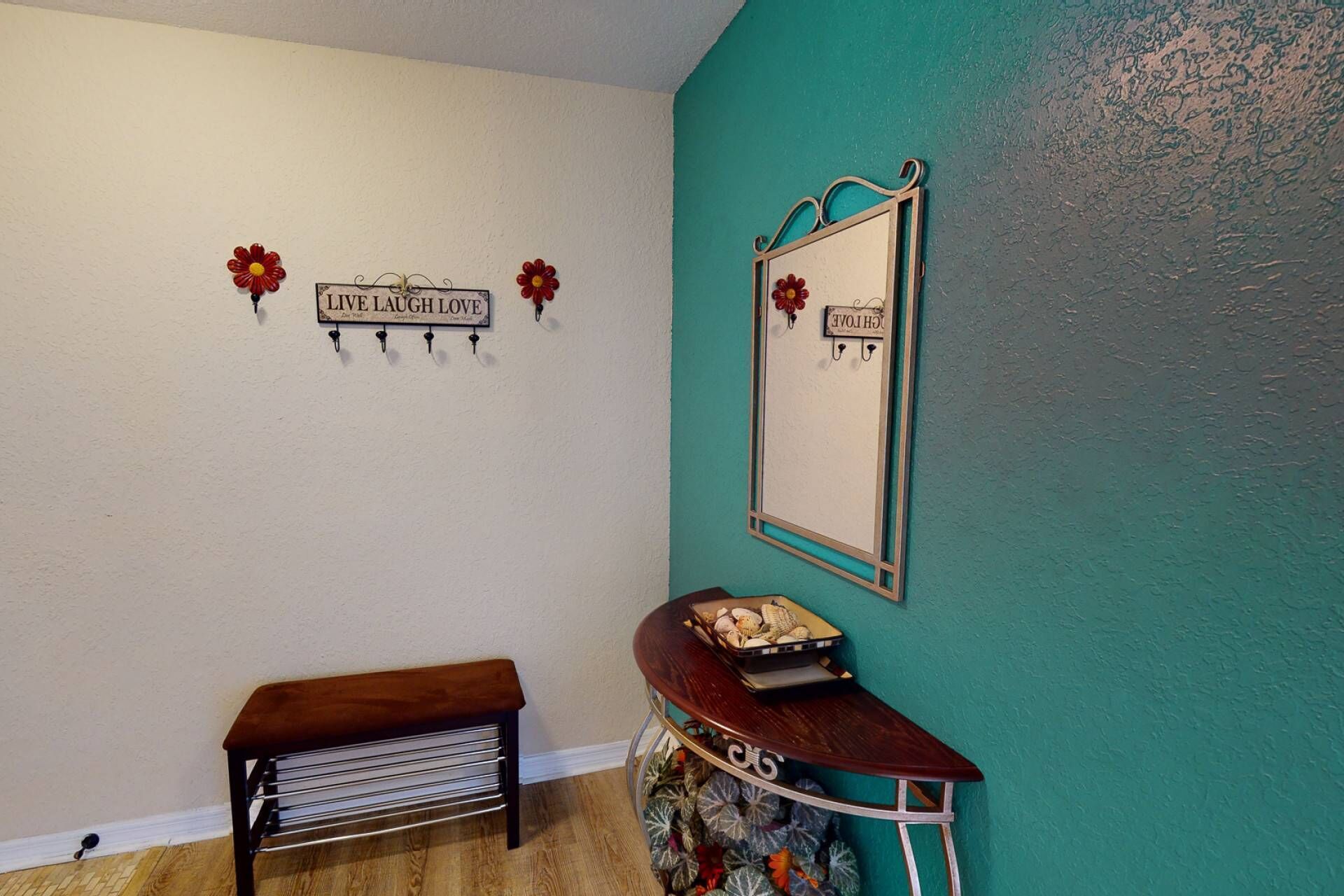 A room with teal walls, a wooden bench, a small table with decorative items, and a mirror with a floral design.