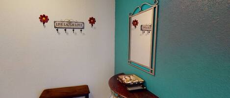 A room with teal walls, a wooden bench, a small table with decorative items, and a mirror with a floral design.