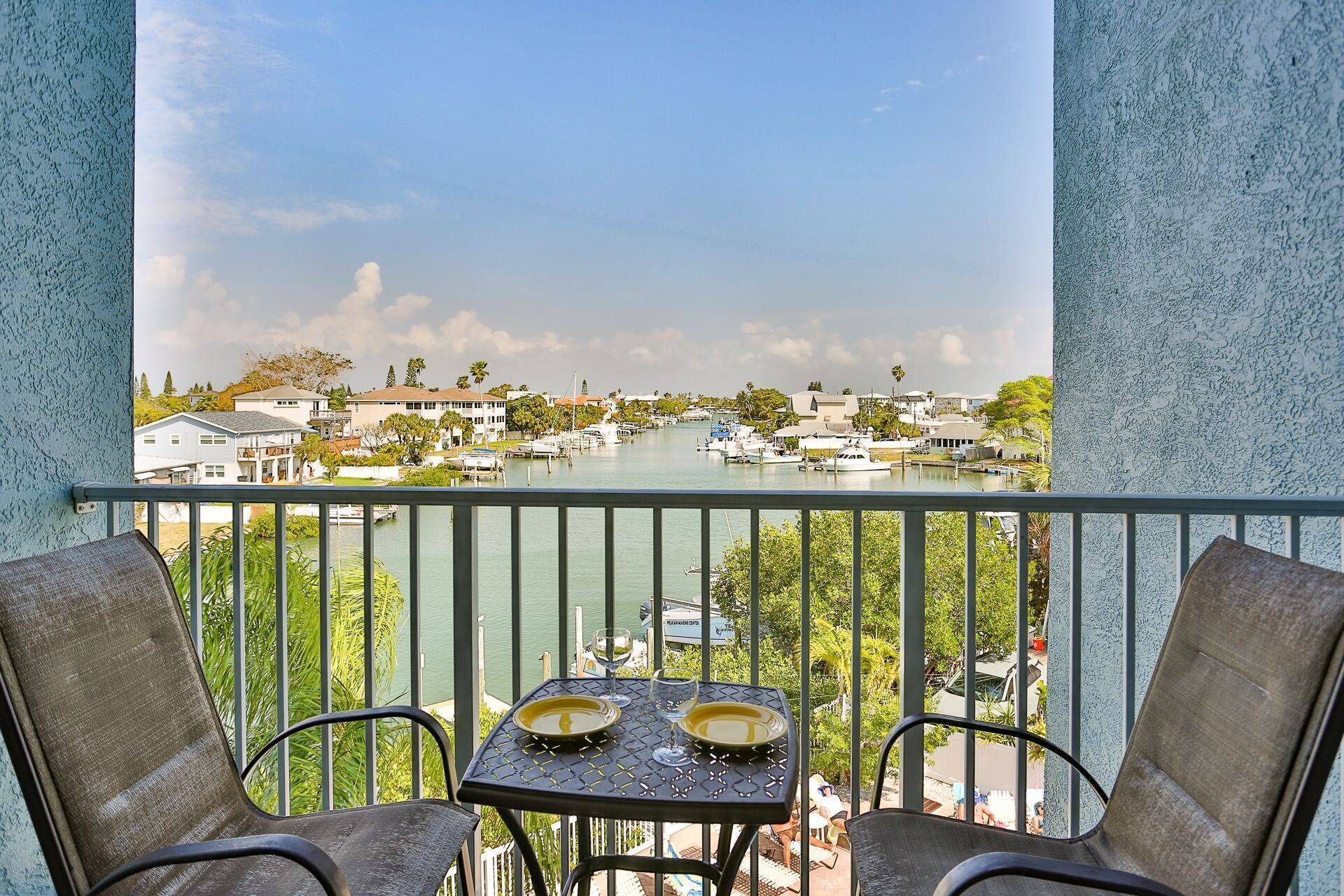 Varanda com duas cadeiras e uma mesa, vista para uma marina com barcos e casas.