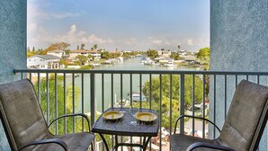 Een balkon met twee stoelen en een tafel, met uitzicht op een jachthaven met boten en huizen.