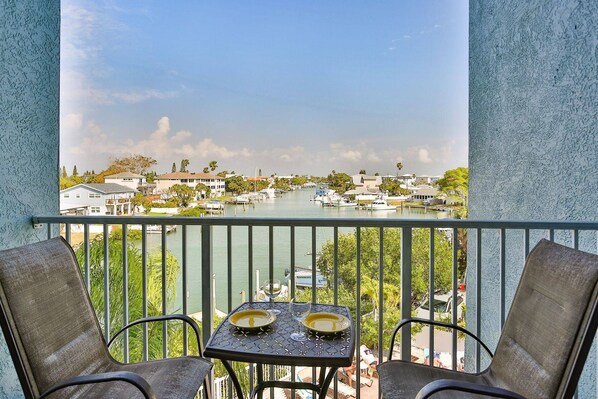 A balcony with two chairs and a table, overlooking a marina with boats and houses.