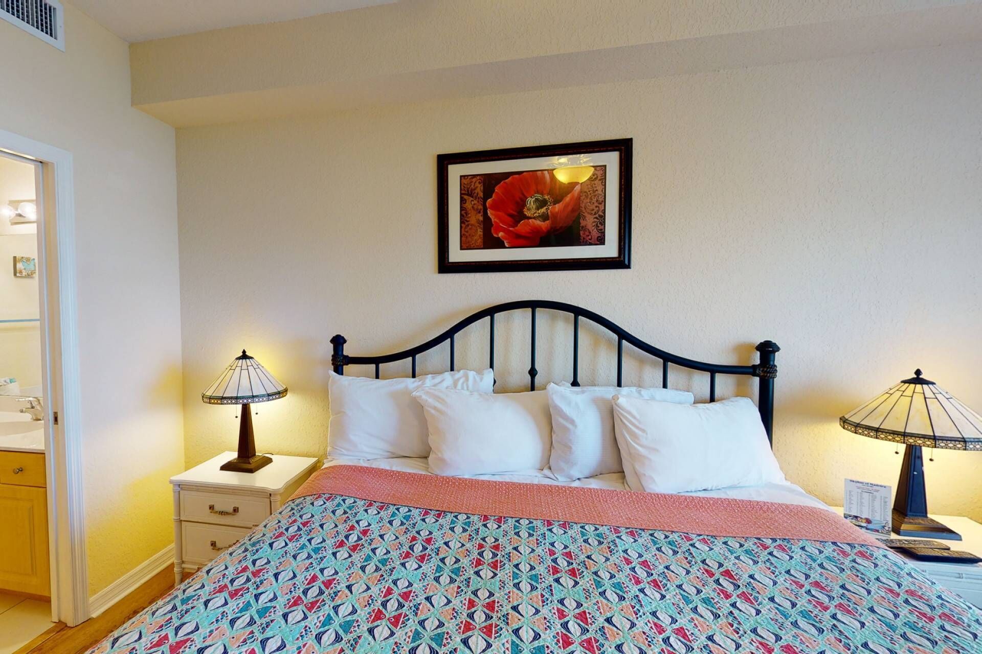 A neatly made bed with white linens, a patterned bedspread, and two bedside lamps.