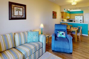 A living room with a striped sofa, a blue armchair, and a kitchen in the background.