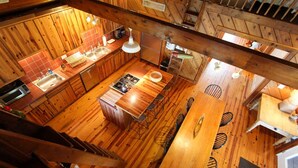 Interior de una cabaña de madera con cocina, comedor y escalera.