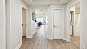 Un couloir doté d’un plancher en bois et de murs blancs, qui mène à un espace cuisine comprenant une table à manger et des chaises.
