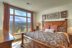 A bedroom with a large window, a wooden bed, and three framed pictures on the wall.