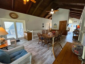A spacious dining area with a wooden table and chairs, a ceiling fan, and a view of the outside through large windows.
