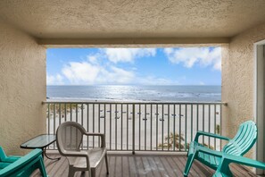A balcony with a view of the ocean, two green chairs, a table, and a chair with a mesh backrest. - Direct Beachfront - 3b 2b - Beach Place #411 (Madeira Beach)