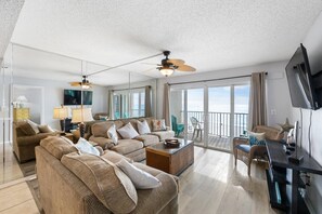 A spacious living room with a large sofa, a coffee table, and a TV. There is a balcony with a view of the ocean. - Direct Beachfront - 3b 2b - Beach Place #411 (Madeira Beach)
